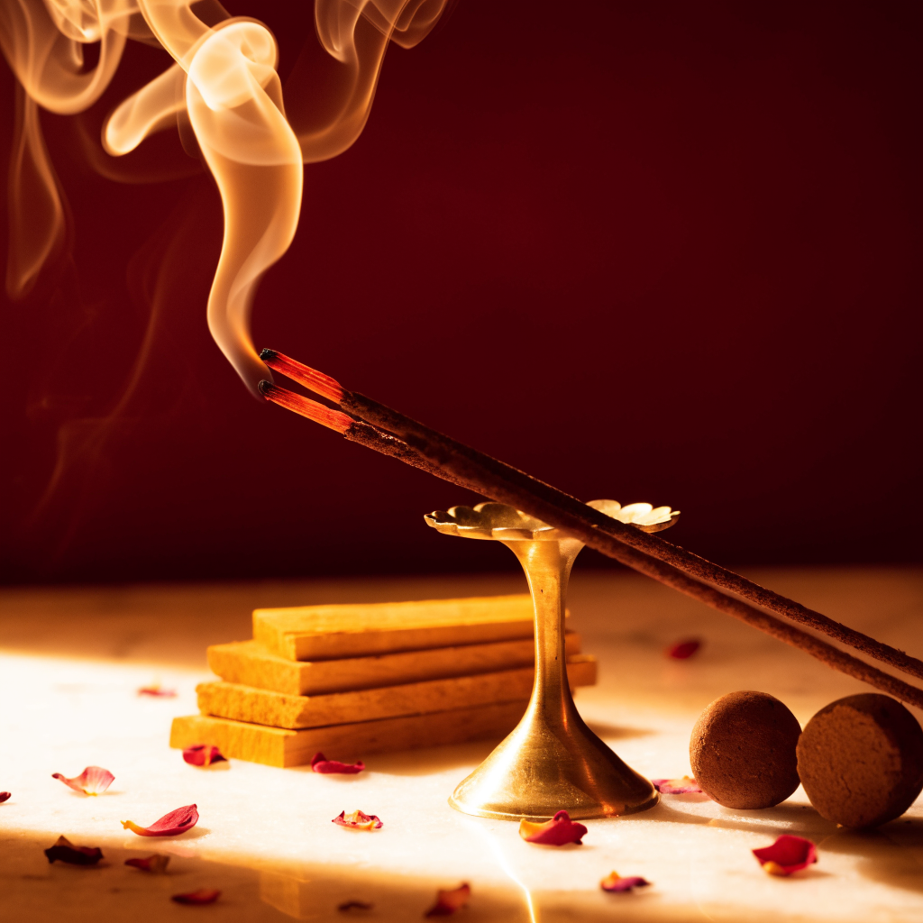 Burning agarbatti incense sticks in a brass holder with dhoop cones and rose petals
