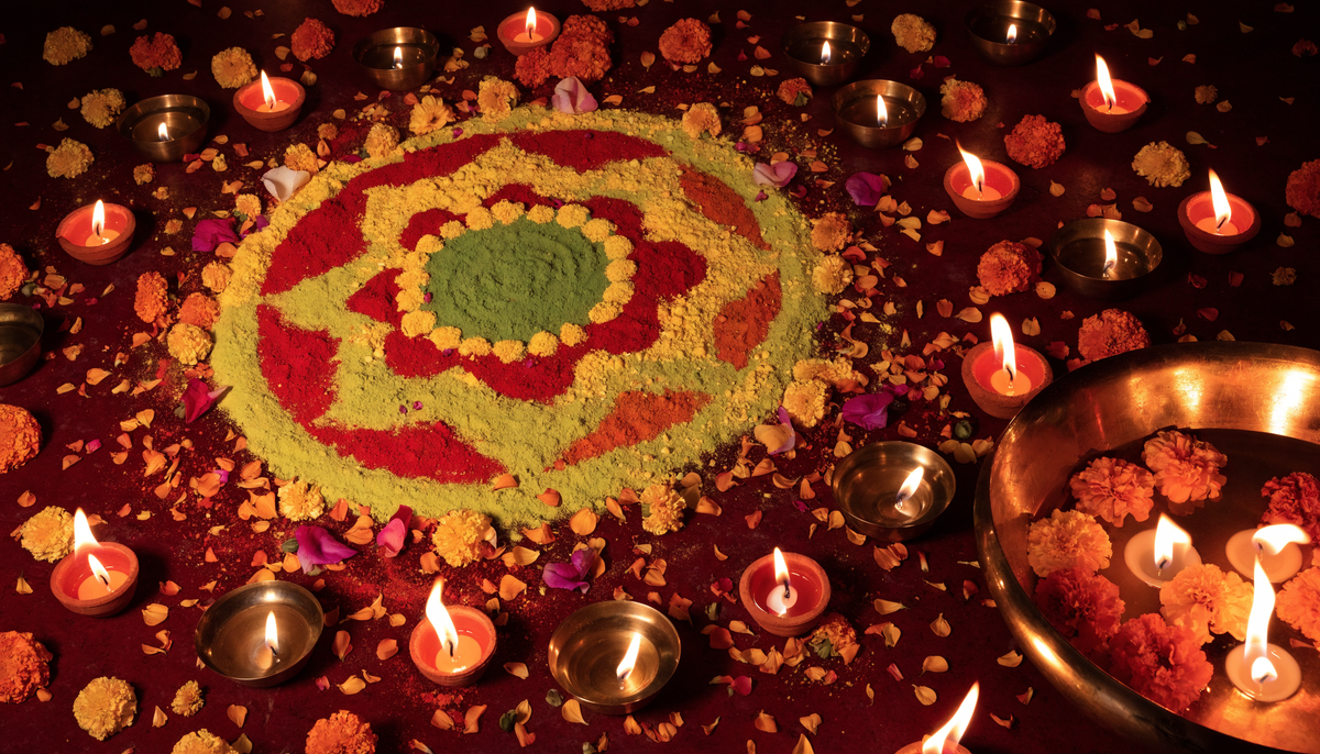 Diwali rangoli surrounded by lit diyas, marigolds and a brass urli